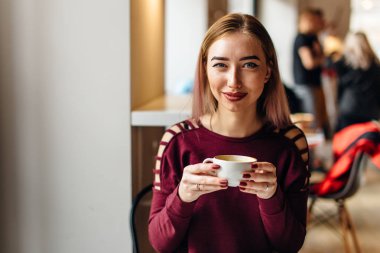 Genç kız oturup fincan kahve ve kamera için bir gülümseme ile