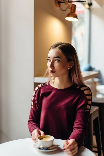 Menina jovem sentar com xícara de café e sorrir para a câmera — Fotografia de Stock