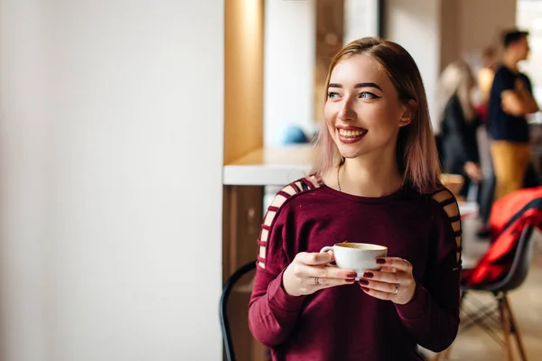 Genç kız oturup fincan kahve ve kamera için bir gülümseme ile — Stok fotoğraf