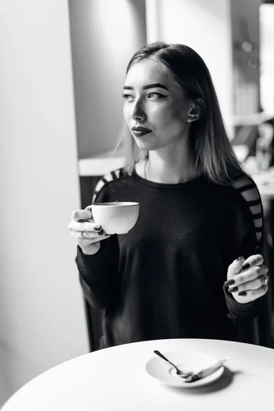 Genç kız oturup fincan kahve ve kamera için bir gülümseme ile — Stok fotoğraf