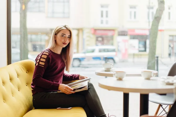 Junges Mädchen sitzt mit Tasse Kaffee und lächelt in die Kamera — Stockfoto