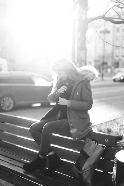 年轻漂亮的女孩坐在长凳上。一只手挂着她的围巾 — 图库照片