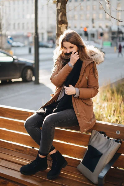 Jeune jolie fille assise sur le banc. Suspendez son écharpe dans une main un — Photo