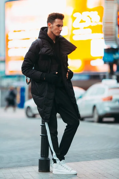 Hombre de moda de pie en la calle cerca de los edificios. Luces de neón —  Fotos de Stock