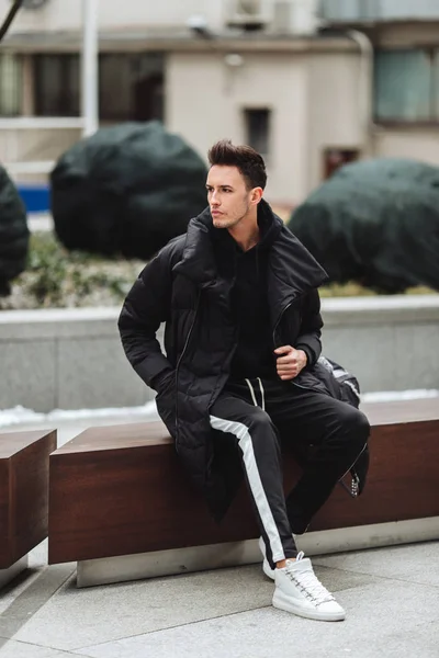 Traje moderno. Hombre de moda sentarse en el banco y mirar a su alrededor . —  Fotos de Stock