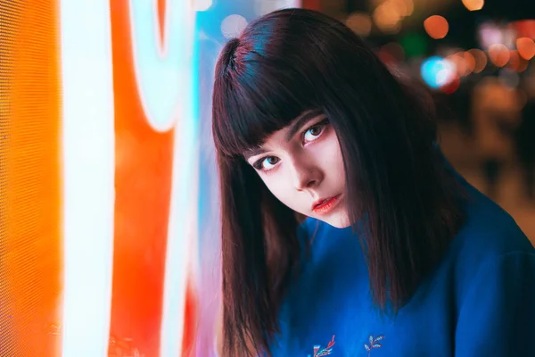 Young Japanese girl stand near neon lights and pose to the camer