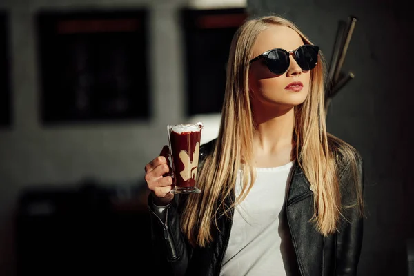 Hezká dívka drží šálek lahodné kávy a waer s brýlemi. Slunce — Stock fotografie