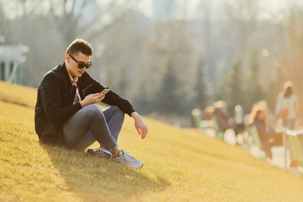 Yonug garçon assis sur l'herbe, porter des lunettes et du texte sur son pho — Photo