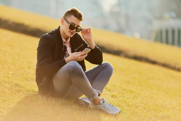 Yonug garçon assis sur l'herbe, porter des lunettes et du texte sur son pho — Photo