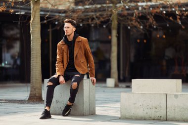 Model görünümlü bir adam oturup modern park arka planda, bankta lo