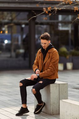 Model görünümlü bir adam oturup modern park arka planda, bankta lo