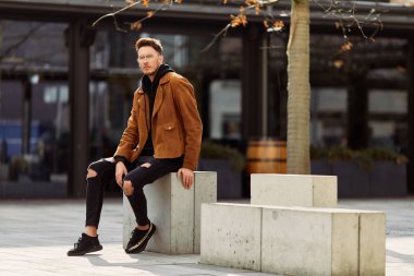 Model görünümlü bir adam oturup modern park arka planda, bankta lo