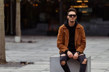 Model görünümlü bir adam oturup modern park arka planda, bankta lo