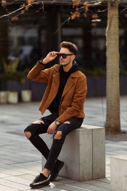 Model görünümlü bir adam oturup modern park arka planda, bankta lo