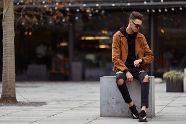 Model görünümlü bir adam oturup modern park arka planda, bankta lo