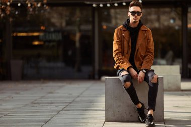 Model görünümlü bir adam oturup modern park arka planda, bankta lo