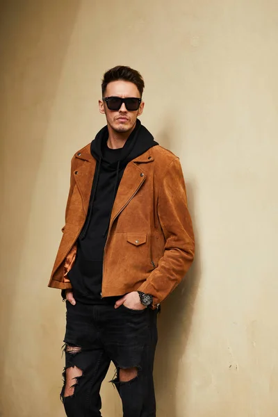 Model looking man stand near the wall and hold his glasses towar