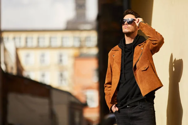 Model looking man stand near the wall and hold his glasses towar