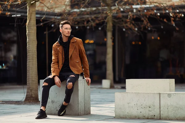 Model görünümlü bir adam oturup modern park arka planda, bankta lo