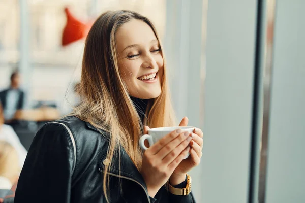 Mooi meisje stand in de buurt van het venster met kopje koffie en glimlach — Stockfoto