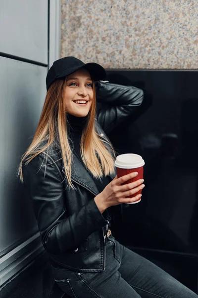 Giovane ragazza in piedi vicino al muro indossare cappello e occhiali e bere — Foto Stock