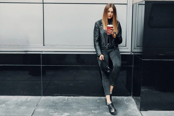 Muchacha joven de pie cerca de la pared de desgaste sombrero y gafas y beber co — Foto de Stock