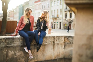 İki kız çeşme üzerinde oturup birbirleriyle konuşmak 