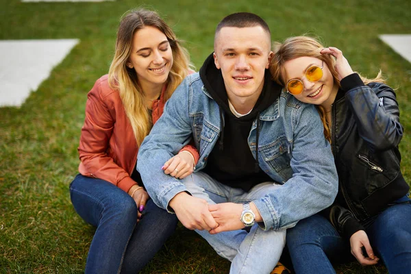 Chico con dos chicas en la hierba verde hablando y sonriendo a Camer —  Fotos de Stock