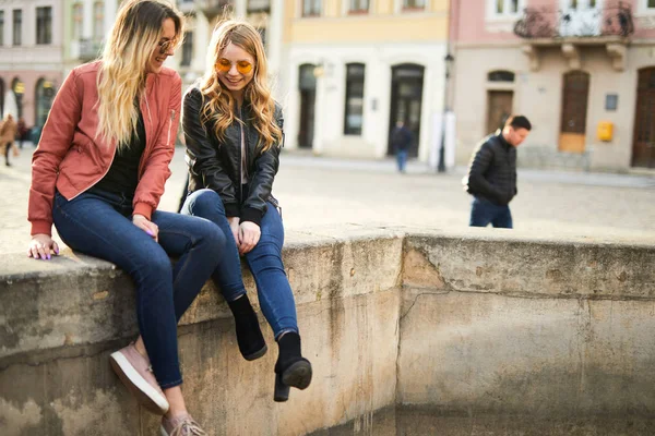 Deux filles s'assoient sur la fontaine et se parlent. — Photo