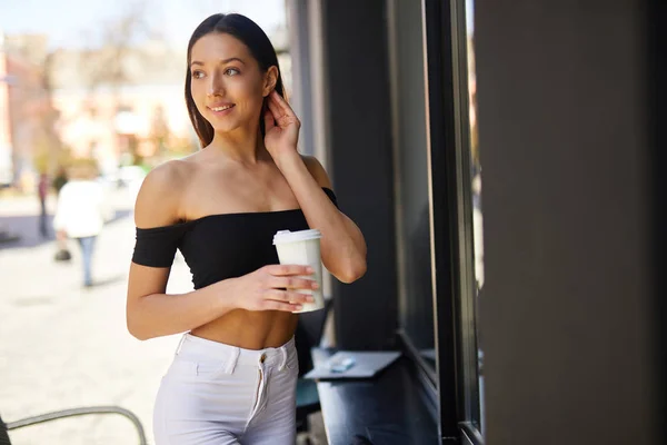 Brunette girl stand on the street look at camera and dring her d