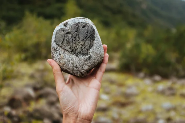 Une fille tenant un rocher avec un cœur à l'arrière-plan des montagnes — Photo