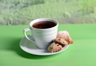 Beyaz fincan da çay. Uçan daire üzerinde kurabiye var. Bir fincan kuru yaprakları, elma ve mandalina yanındaki.