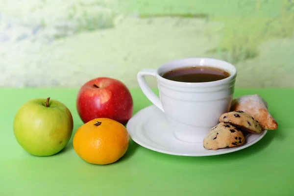 白一杯のお茶。受け皿はクッキーです。乾燥した葉、りんごとみかんのカップの横にあります。. — ストック写真
