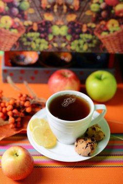 Beyaz bir fincan çay. Fincan beyaz bir daire üzerinde duruyor. Çikolata kurabiye limon parçaları ve bir buket dağ kül Kupası yanındaki vardır.