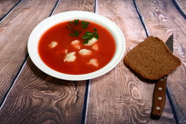 Sopa de tomate com ervas no prato branco. Um pedaço de pão preto deitado perto da placa . Fotos De Bancos De Imagens Sem Royalties