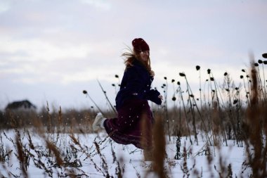 Genç sarışın kız bir yelek ve karla kaplı alan ve oturur üzerinde sonraki için ahşap bir ev yürüme uzun etek.