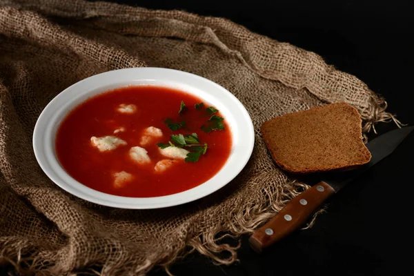 Sopa de tomate com ervas no prato branco. Um pedaço de pão preto deitado perto da placa . Fotos De Bancos De Imagens