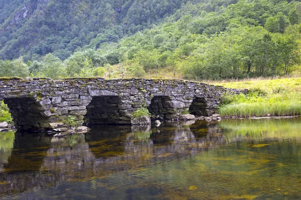 在一个小山谷里，一座古老的石桥穿过一条河. — 图库照片