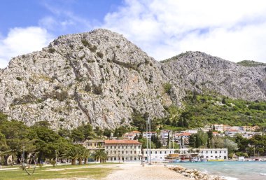 Dağa ve Adriyatik Denizi 'ndeki Omis kasabasına bakın. Önde bir park ve içinde gemiler olan küçük bir liman var. Omis, Hırvatistan 'ın Dalmaçya bölgesinde bulunan bir liman ve kasabadır.