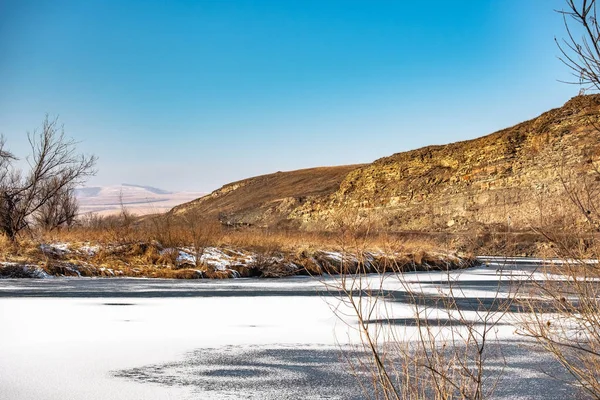 Krajina, zamrzlá řeka břeh, stromy a tráva ve sněhu — Stock fotografie