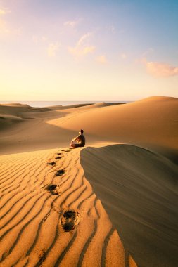 Man sitting and relaxing on sand dunes by the sunrise, in Maspalomas on Gran Canaria. clipart