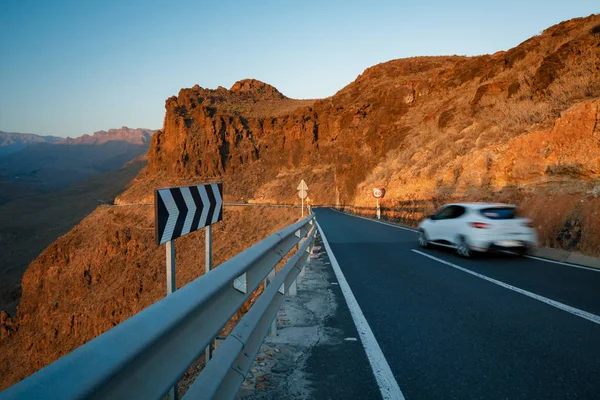 在日落之光的大加那利岛山峰之间的公路上行驶的汽车 — 图库照片