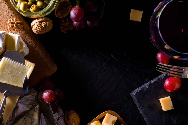 Palette of many types of cheese and some grapes, olives and wine with copy space.