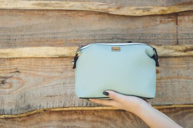 Ahşap arka planda mavi el çantası tutan bir kadın.