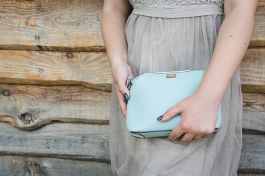 Kız ahşap arka planda mavi el çantası tutuyor. Küçük bir kadın hentbası