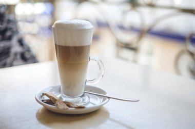 Tahta masada bir bardak sıcak latte ve şeker.