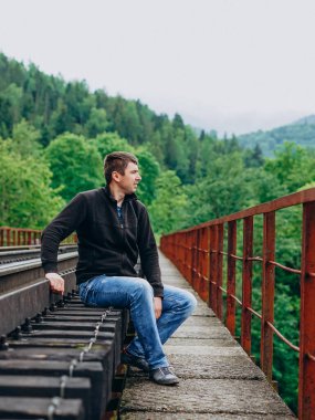 Kot pantolonlu bir adam tren yolunda oturur..