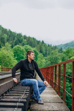 Kot pantolonlu bir adam tren yolunda oturur..