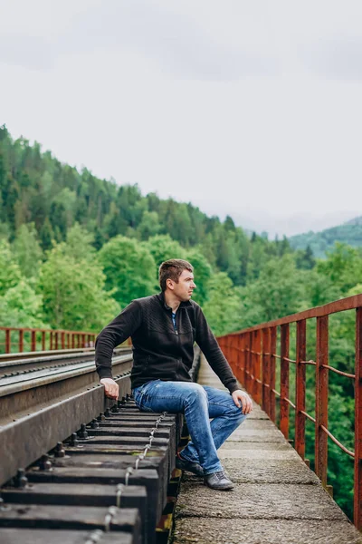 Kot pantolonlu bir adam tren yolunda oturur..