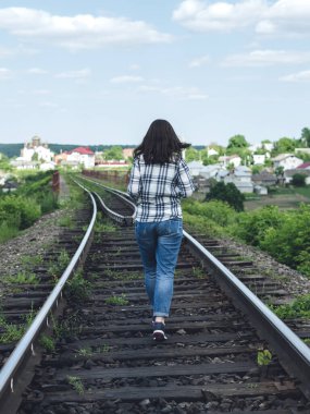 Kotlu ve gömlekli genç bir kadın güneşli bir günde tren yolu boyunca koşuyor.
